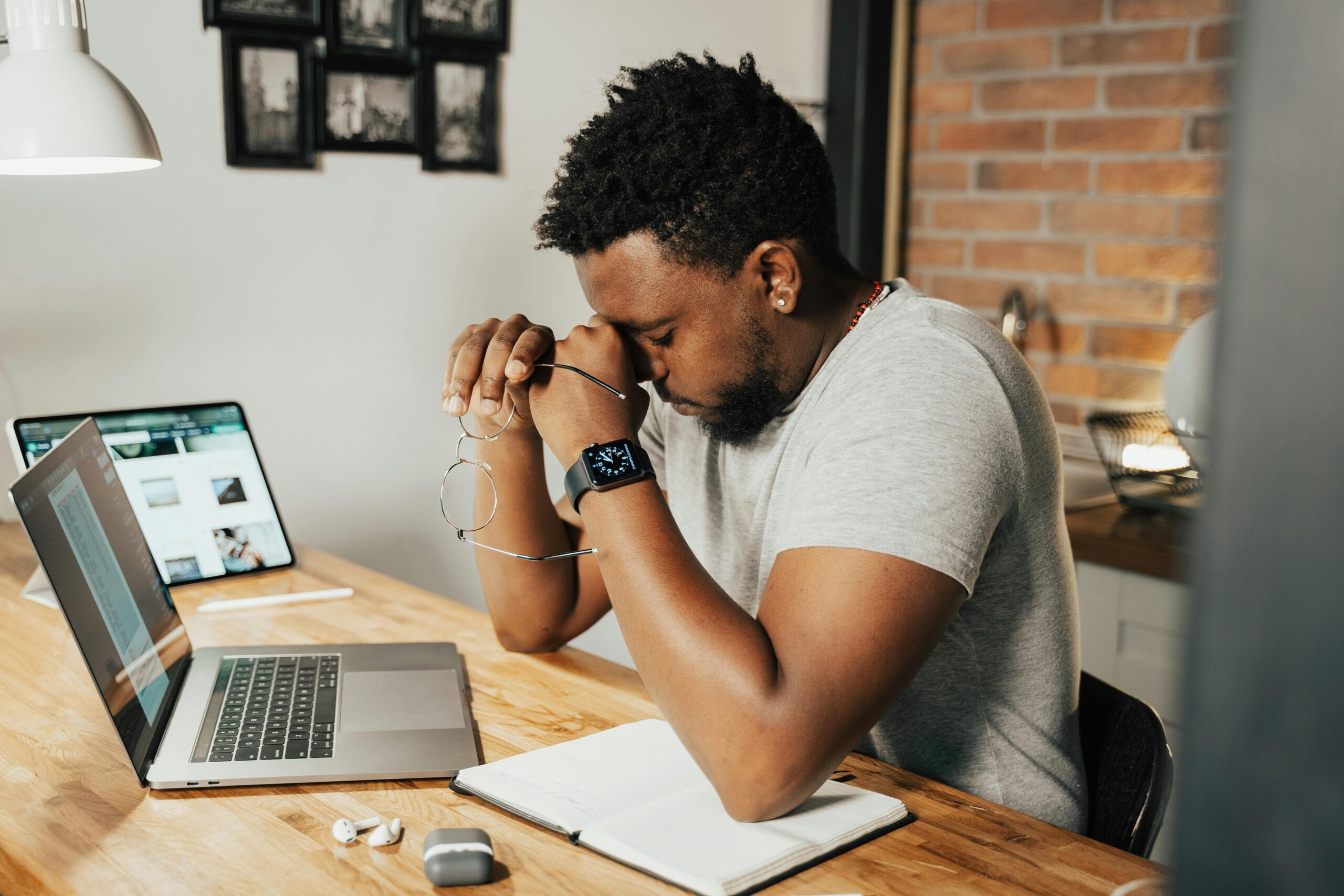 Exhausted man sitting at home desk with laptop and digital devices, representing remote work challenges.